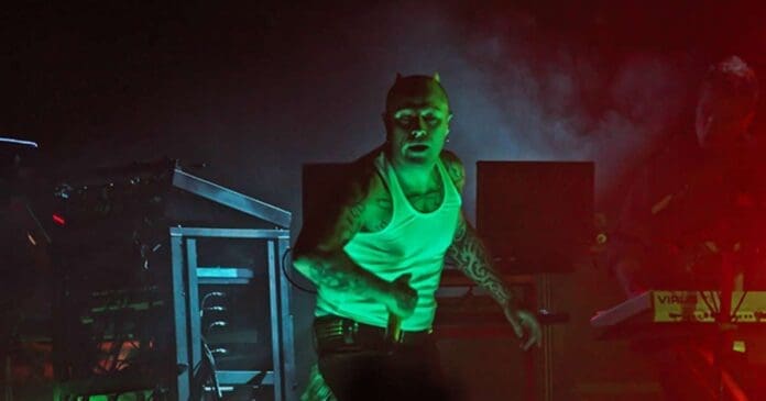 A man on stage with a green light behind him passionately performing the lyrics to 