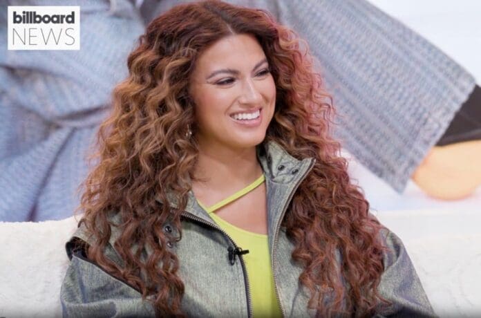 Tori Kelly, a woman with curly hair, sitting on a couch.