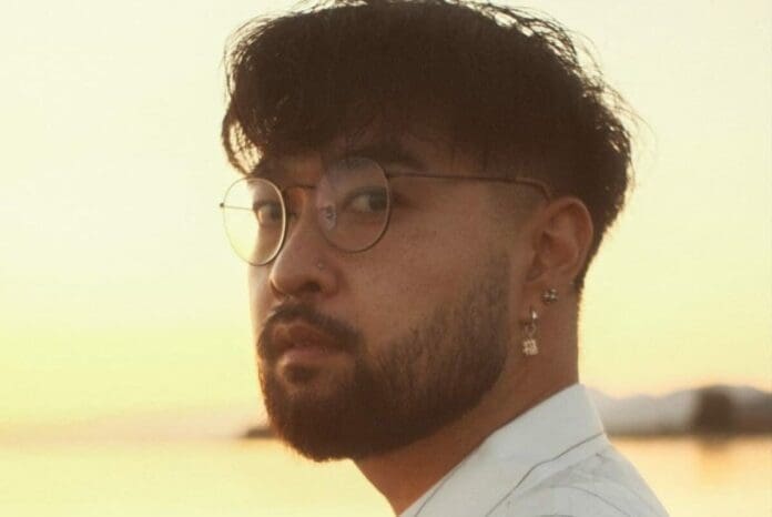 A man with glasses and a beard enjoying the Zensei Lounge-Meets-Downtempo EP on his headphones while standing in front of the breathtaking ocean.