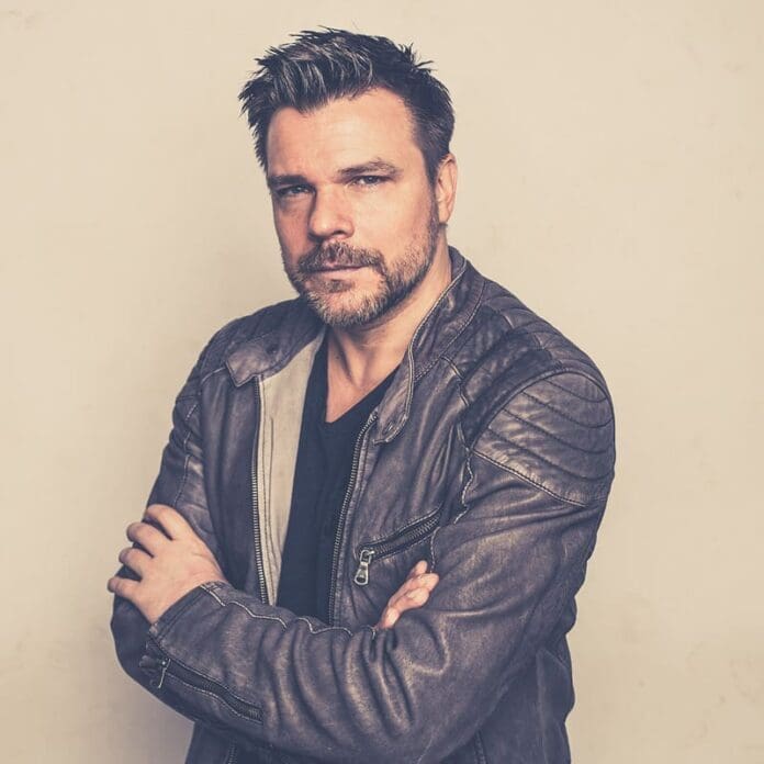 A man in a leather jacket posing with his arms crossed, giving off an ATB vibe.