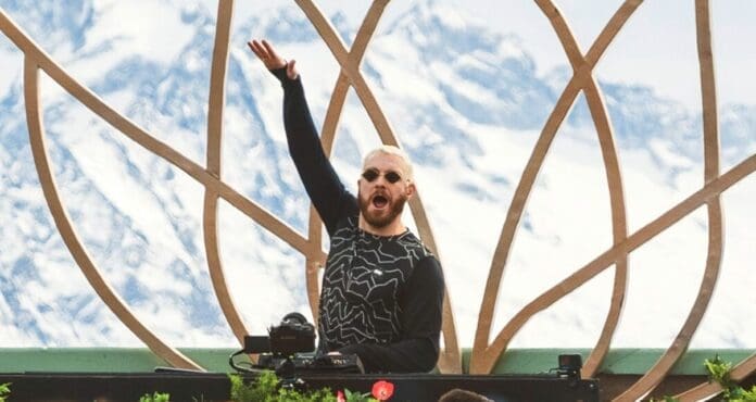 A DJ with his hands up in the air, showcasing DJ tricks and creating James Hype moments against the stunning backdrop of a mountain.