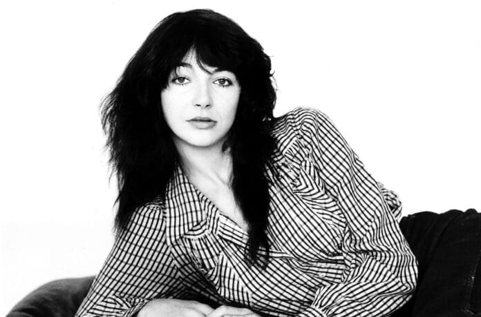 A black and white photo of Kate Bush posing on a couch.