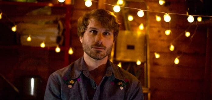 Max Norton, an indie artist, contemplatively stands in front of a string of lights while connecting with deep emotions for his debut single.