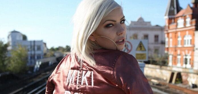 A beautiful blonde woman wearing a red bomber jacket, styled by Miki Rose.